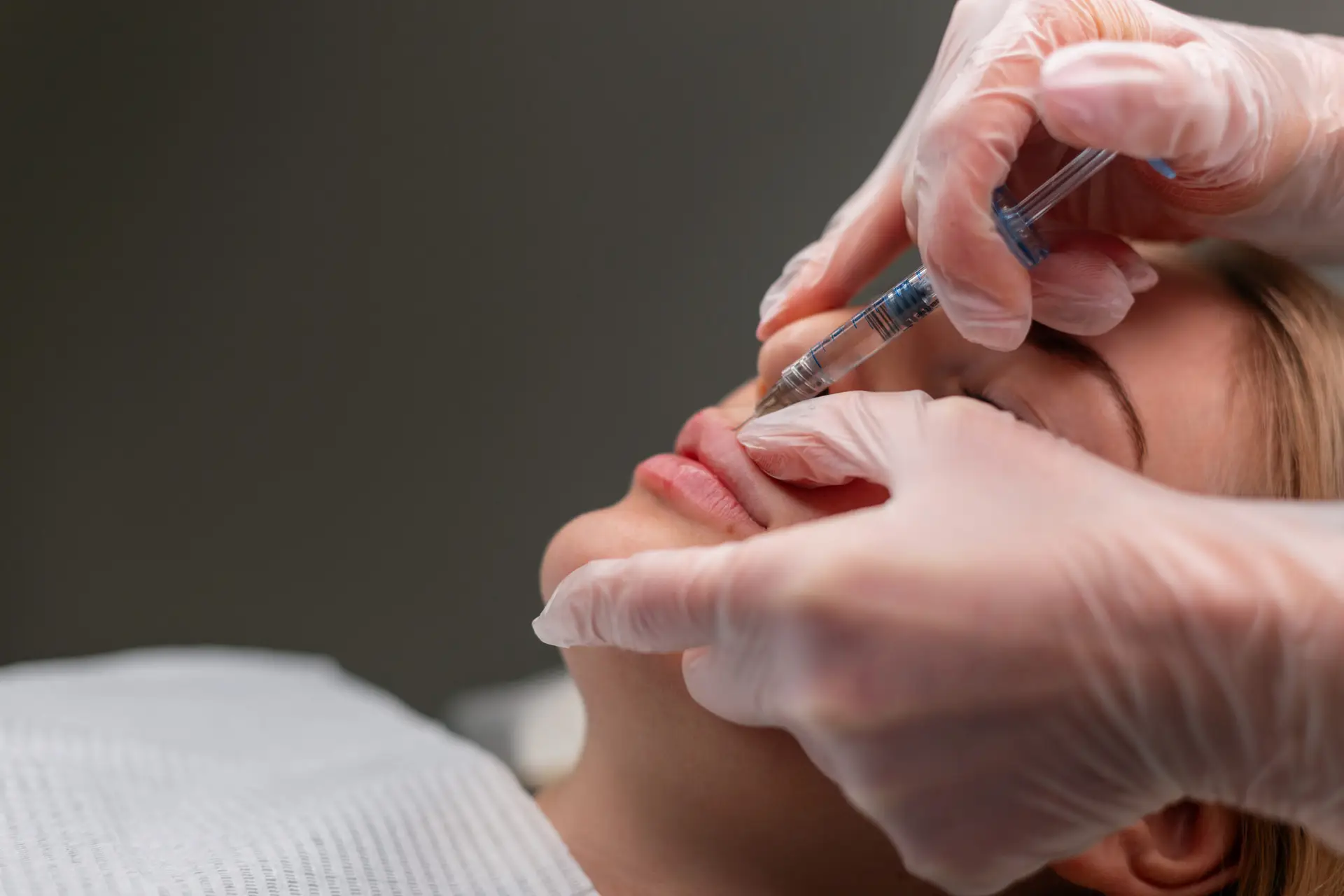 professional cosmetologist woman doing lip augmentation correction procedures in beauty clinic. girl doing filler injection in lip
